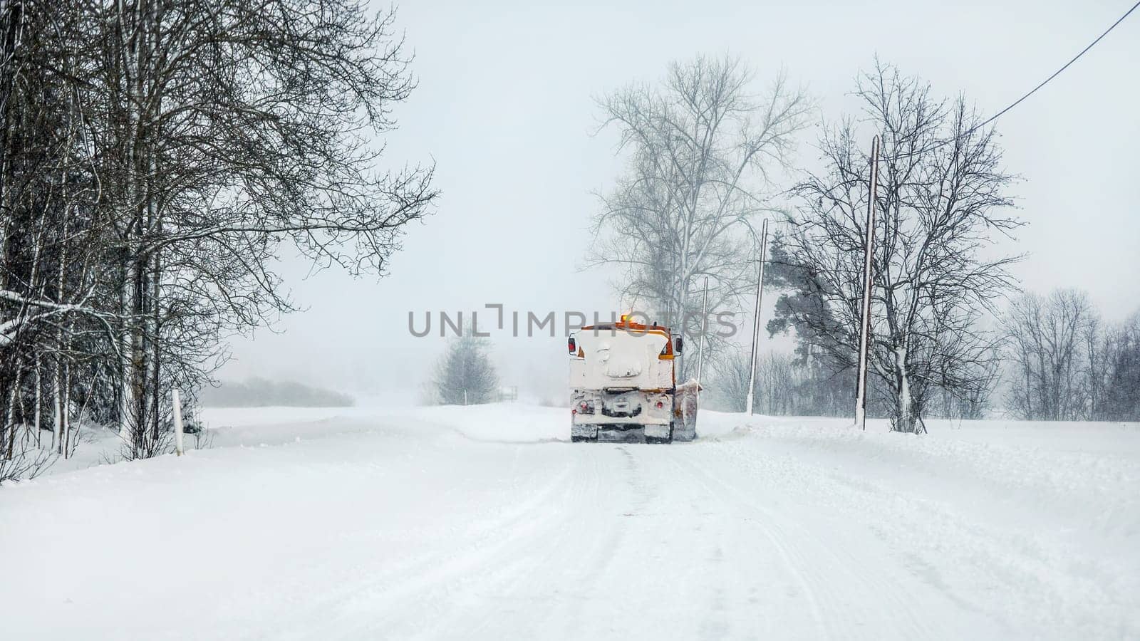 Snowplow highway maintenenace truck cleaning road completely white from snow in winter, dangerous driving conditions, view from car behind. by Ivanko