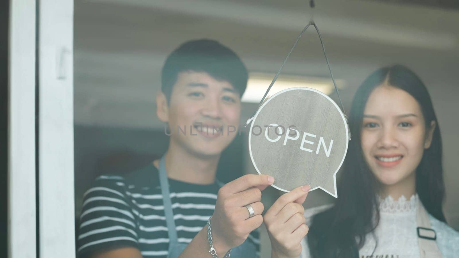 Happy Coffee Shop owner in an apron turning open sign board on glass door. Small business owner opening a small business. by ijeab