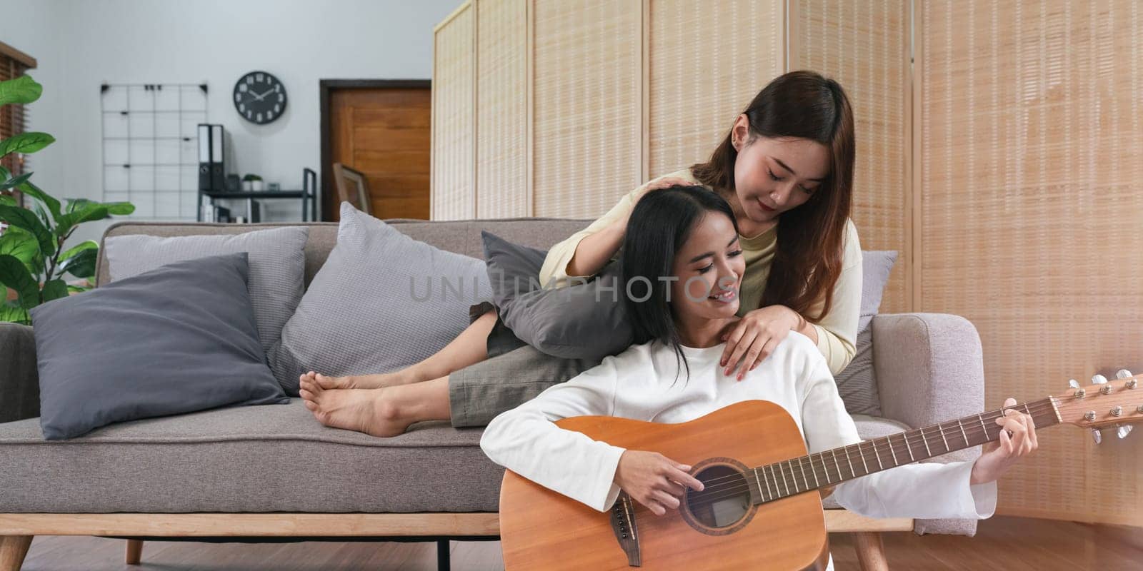 Homosexual LGBT. lesbian couple together concept. Couple of young women playing guitar and singing in living room with happiness moment by nateemee