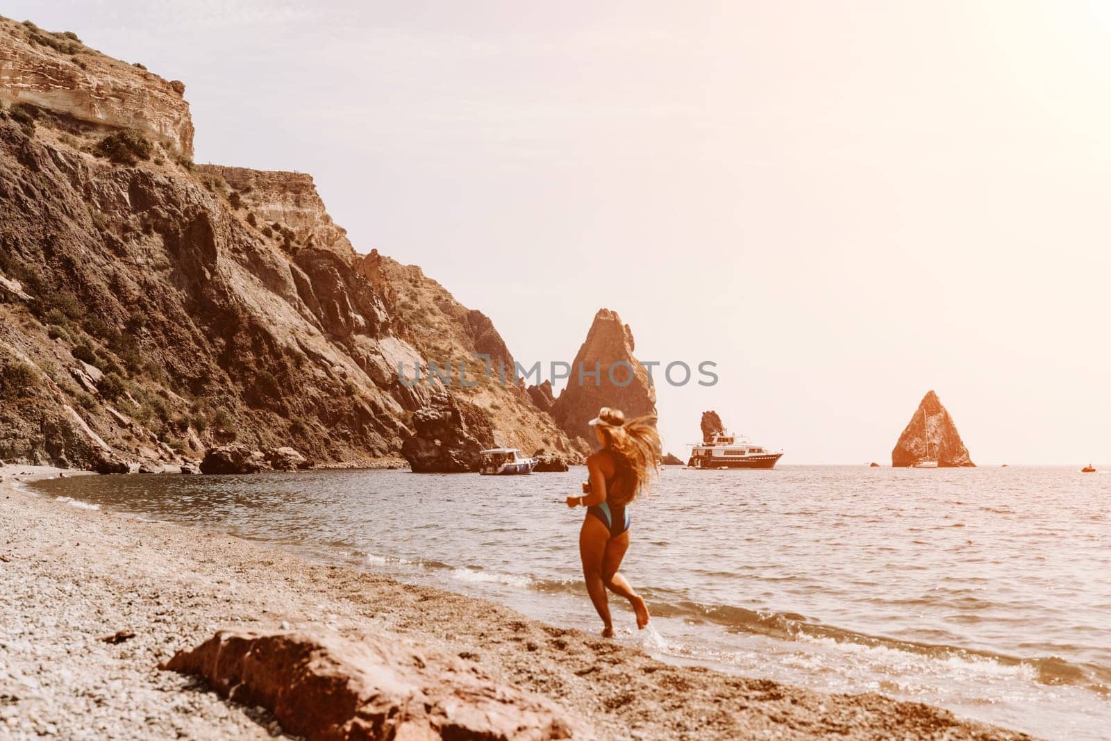 Woman travel summer sea. A happy tourist in a blue bikini enjoying the scenic view of the sea and volcanic mountains while taking pictures to capture the memories of her travel adventure