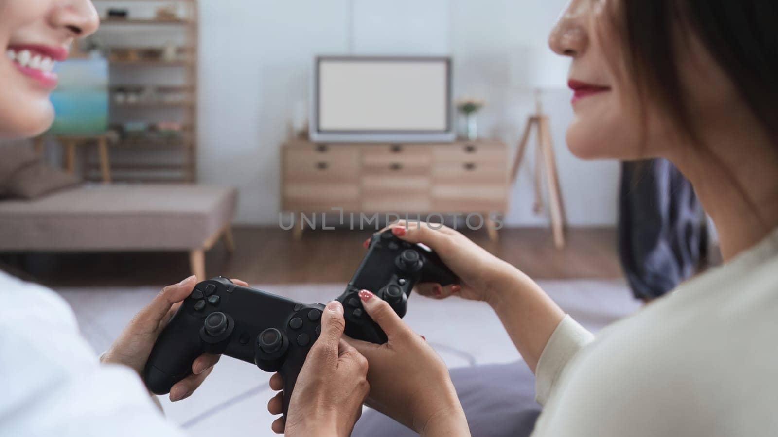 Asian homosexual couple of lesbian woman sitting on couch in living room at home enjoy and excited holding console playing game together by nateemee