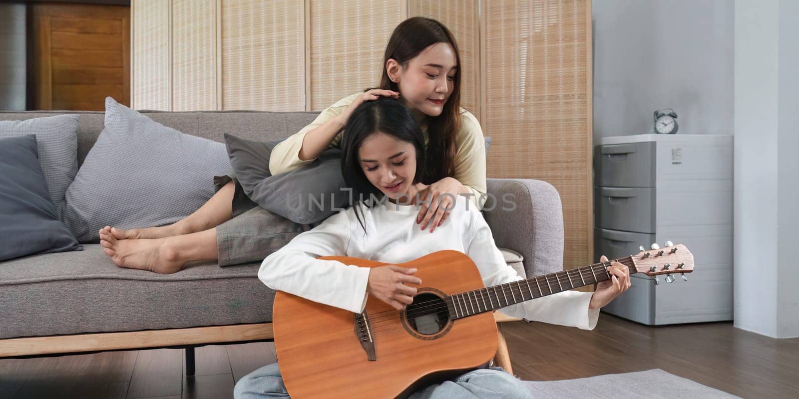 Homosexual LGBT young women playing guitar and singing in living room with happiness moment by nateemee