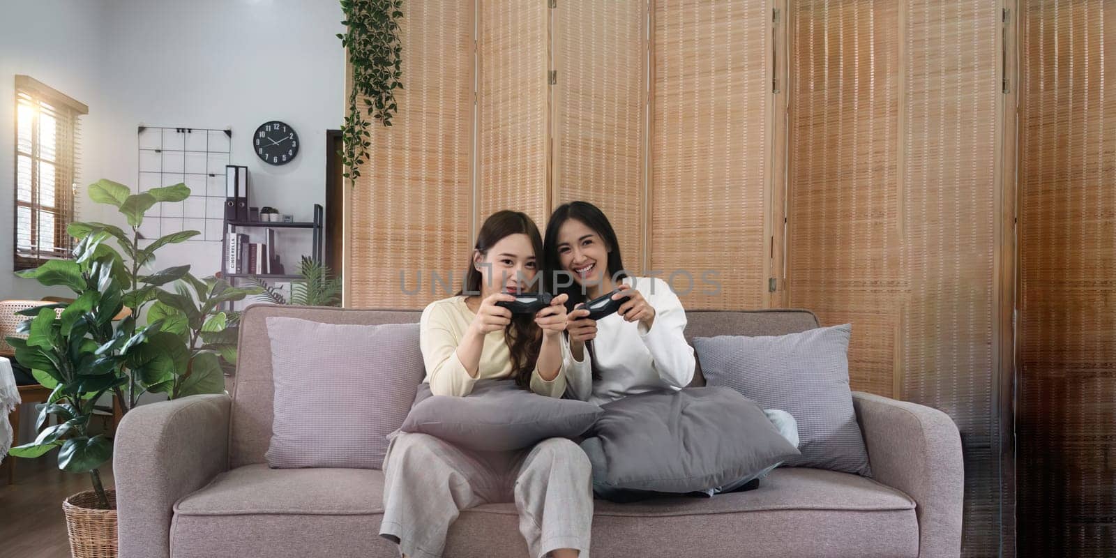 Asian homosexual couple of lesbian woman sitting on couch in living room at home enjoy and excited holding console playing game together.