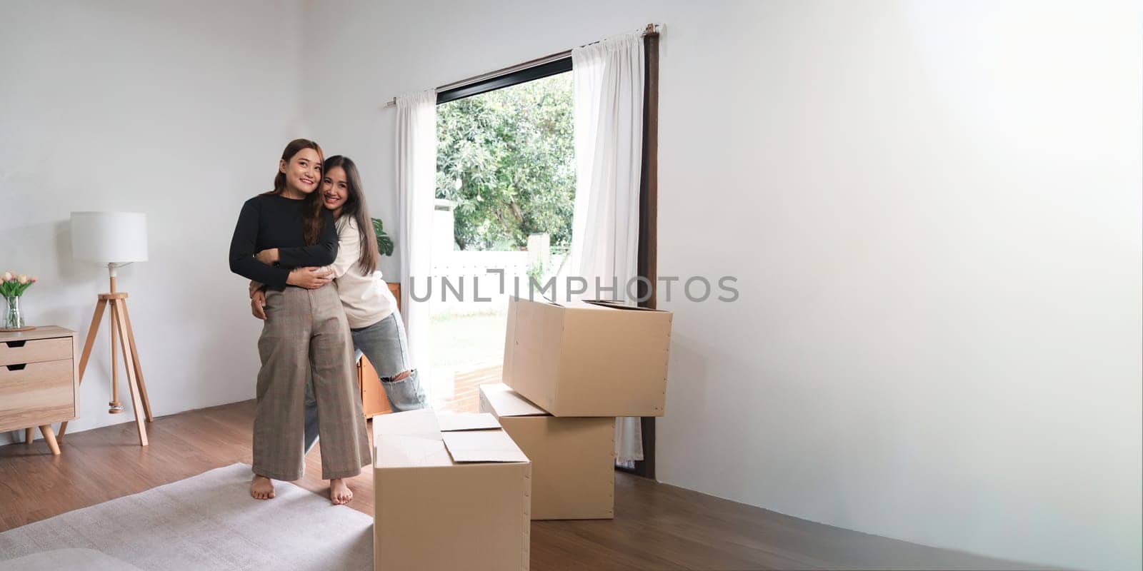 Homosexual happy young Asian woman hug girlfriend after moving stuff to a new rent house.