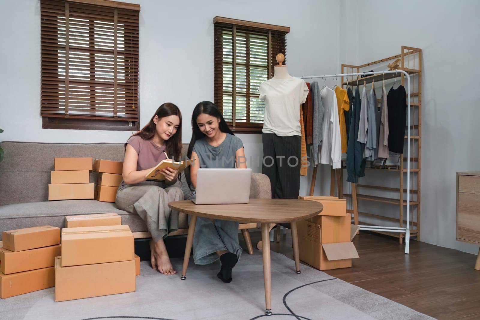 Asian woman friends couple talk to sell the clothes at home. Young attractive business people female take a order clothing to customer in online retail to sales at living room by nateemee