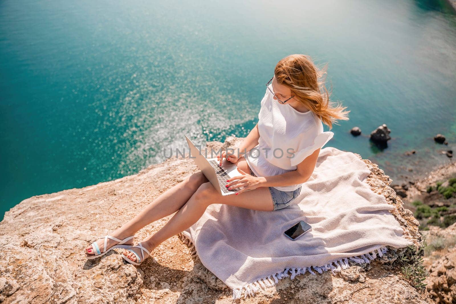 Freelance woman working on a laptop by the sea, typing away on the keyboard while enjoying the beautiful view, highlighting the idea of remote work