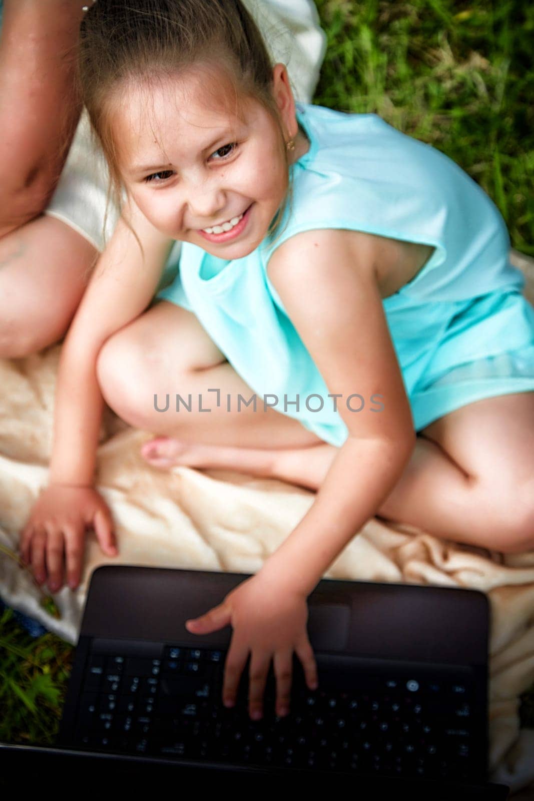 Pretty little funny girl with a laptop on the grass in nature