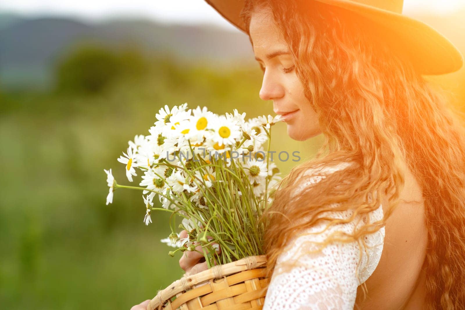 A middle-aged woman in a white dress and brown hat holds a large bouquet of daisies in her hands. Wildflowers for congratulations.