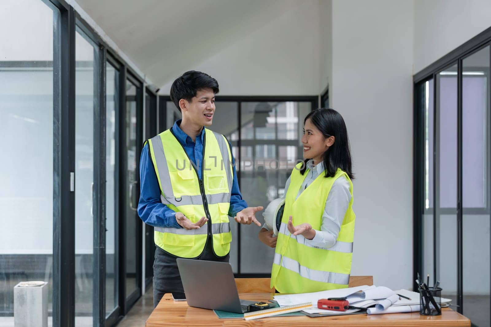 Two young man and woman engineers meeting, working, discussing, planing, designing, measuring layout of building blueprints in construction site floor at factory.