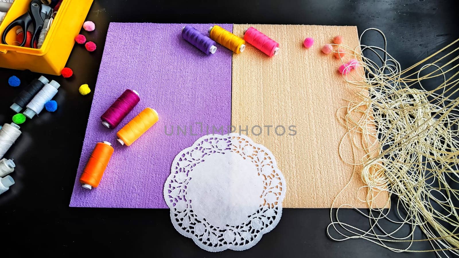 Abstract background with texture and frame with beige and lilac or purple velvet paper, a white napkin, colored spools of treateds and copy space. Top view. Hand made and sewing