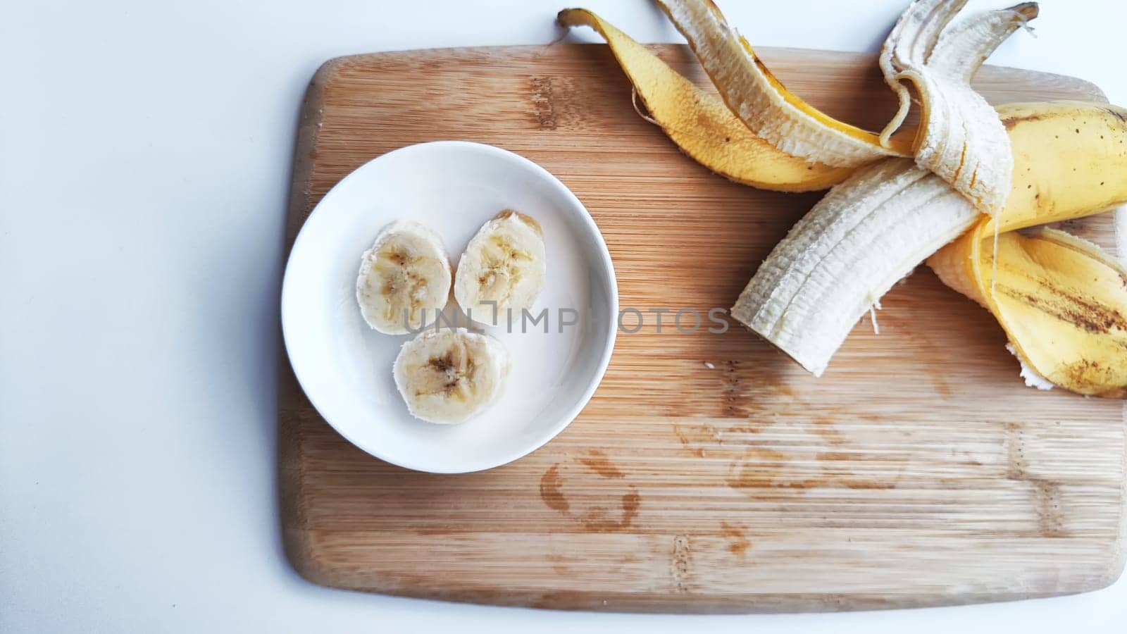 Banana with open panel on wooden board and sliced round pieces on the plate on white background. Ripe banana with peel and cooking. Delicious sweet fruit dessert. Close up