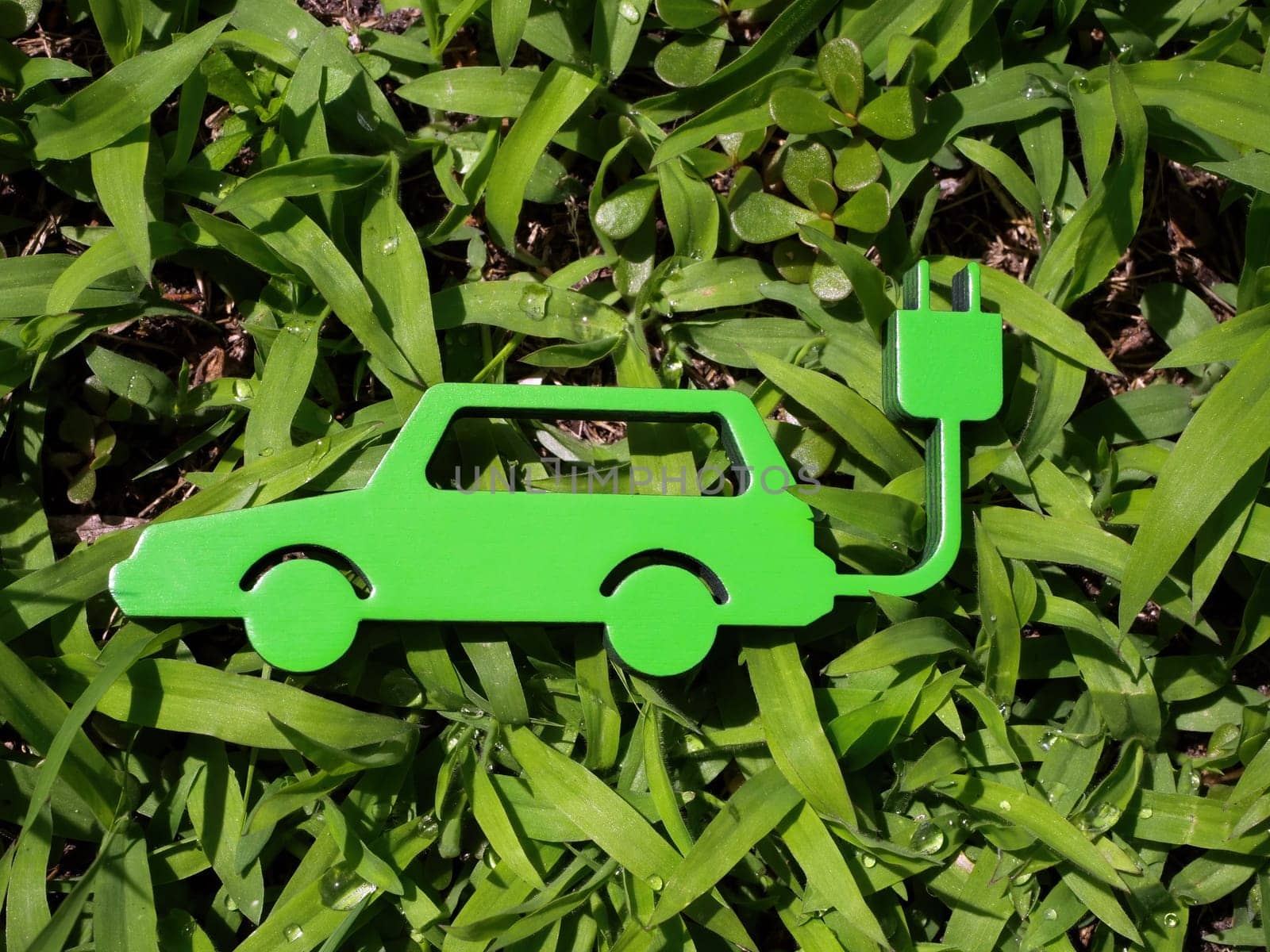 Figurine of the electric car lies on the green grass. Sustainability concept. by designer491