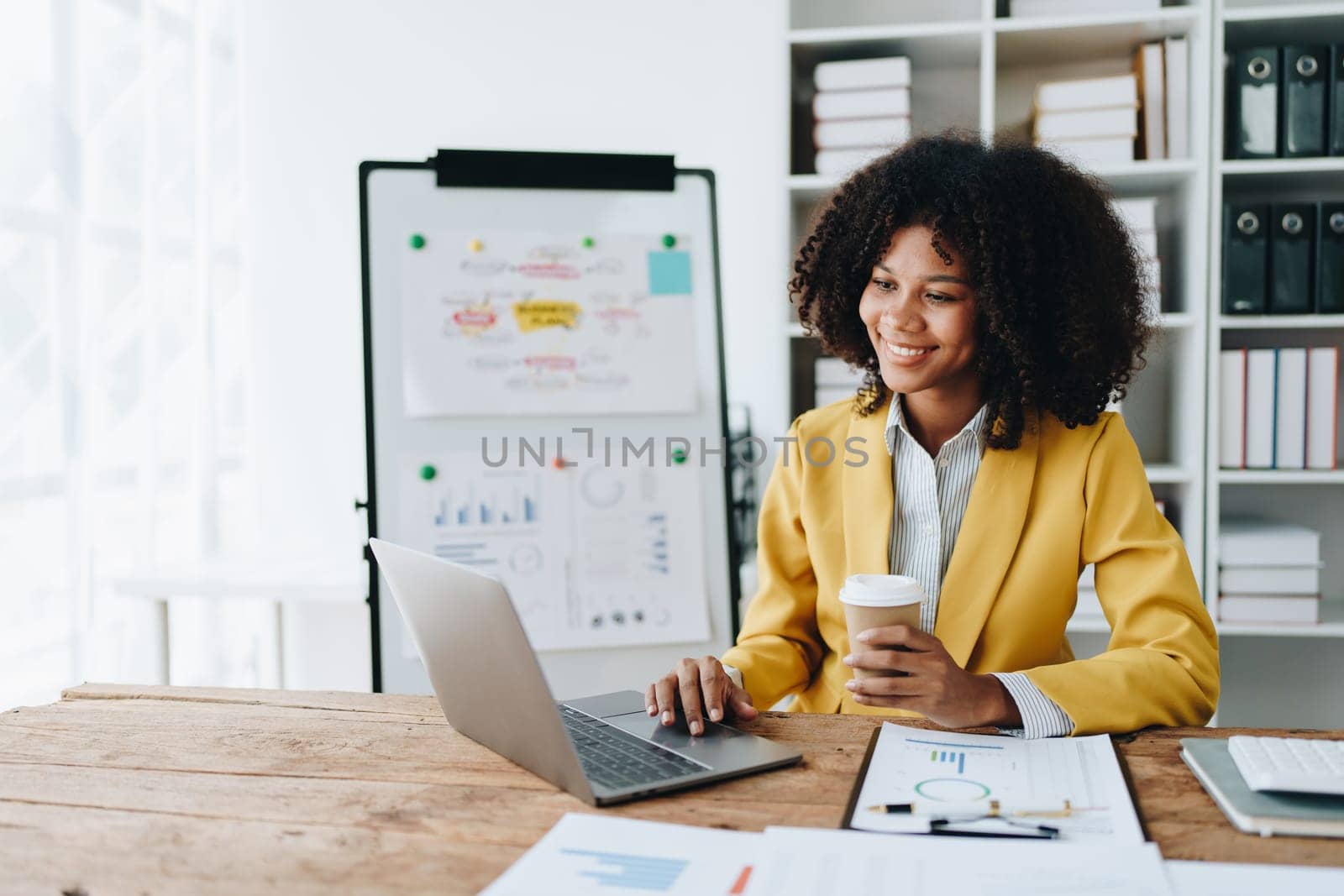 Beautiful young African american businesswoman using laptop computer and paperworks with planning working on financial document, tax, exchange, accounting and Financial advisor by Manastrong