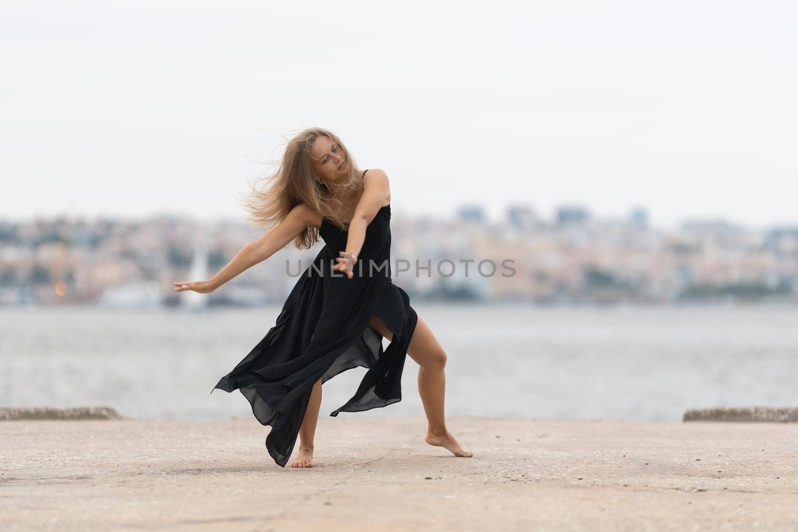 A woman in black dress dancing on the pier. Mid shot