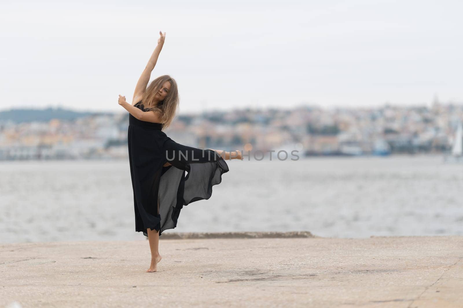 A woman in black dress dancing ballet on the pier. Mid shot