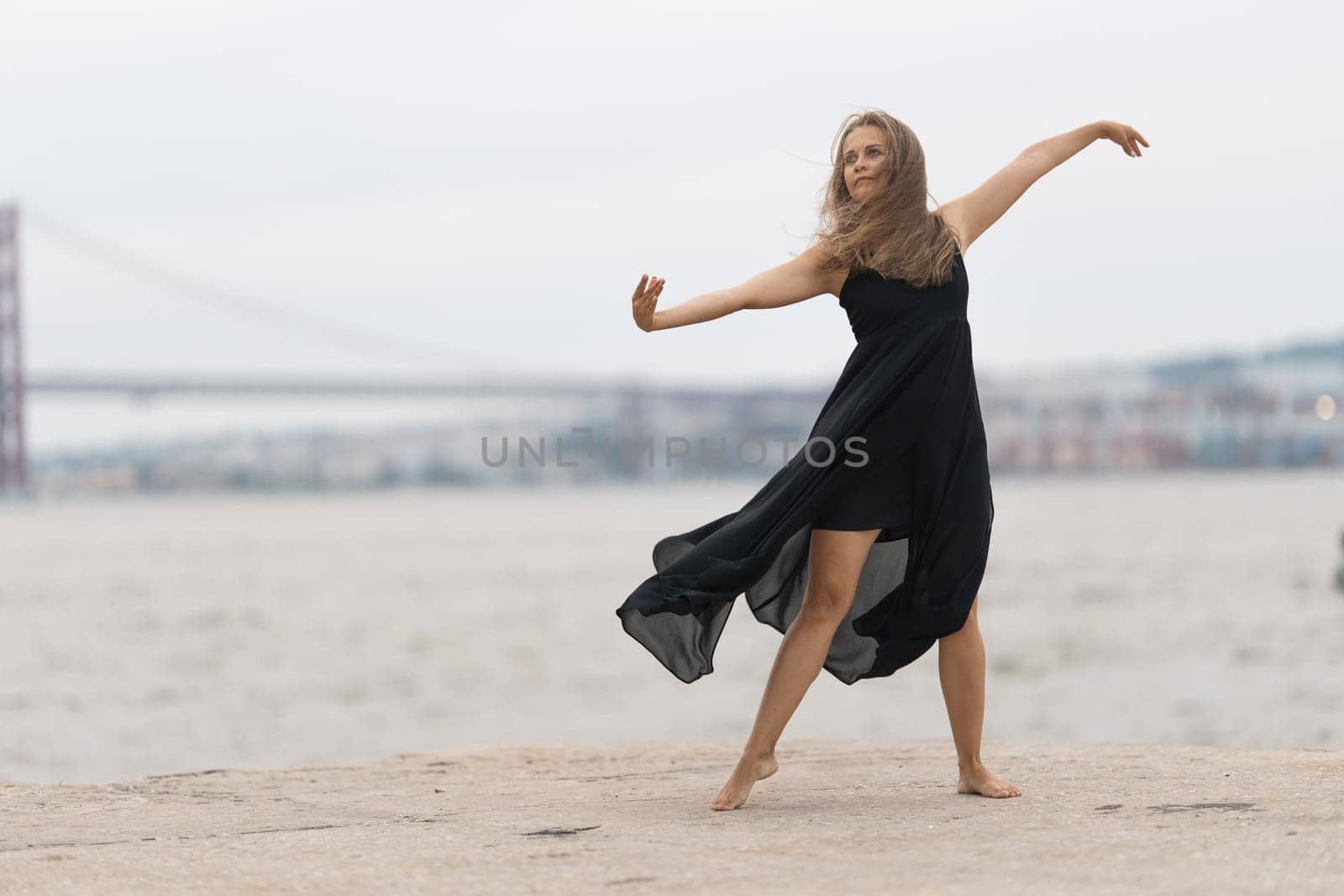 An adult woman in black dress dancing on the pier. Mid shot