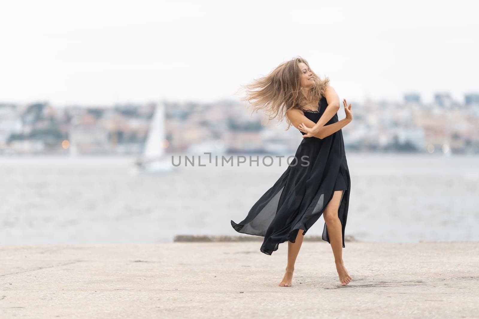 An adult smiling woman in black dress dancing on the pier in cloudy weather by Studia72