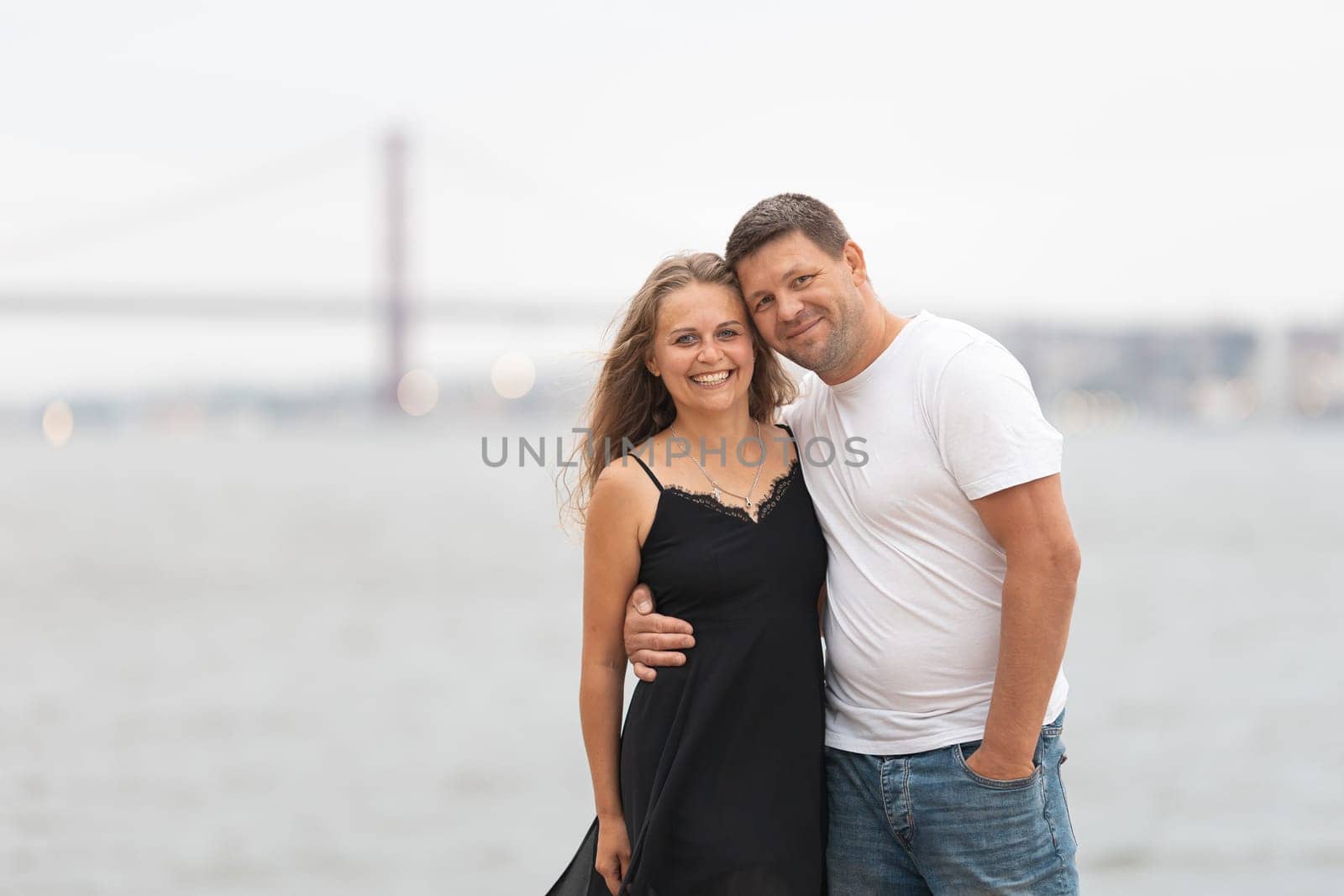 Cute adult married couple standing on the pier - husband holding his wife by waist. Mid shot