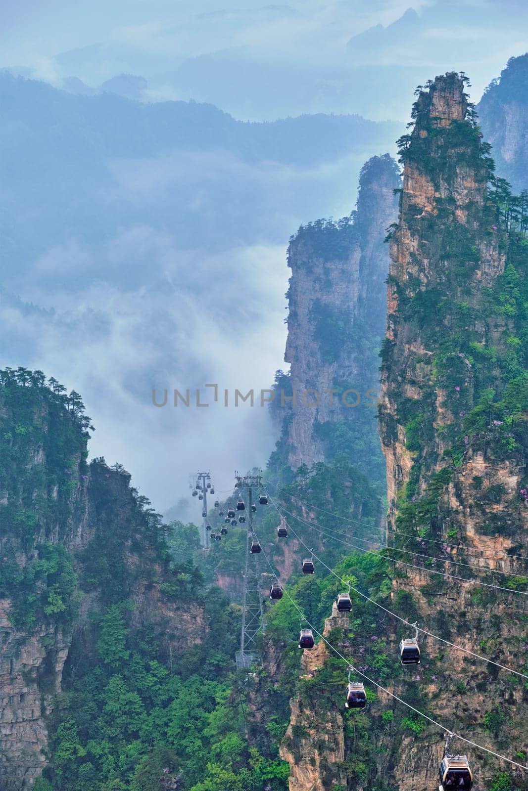 Famous tourist attraction of China - Zhangjiajie stone pillars cliff mountains in fog clouds with cable railway car lift at Wulingyuan, Hunan, China. With camera pan