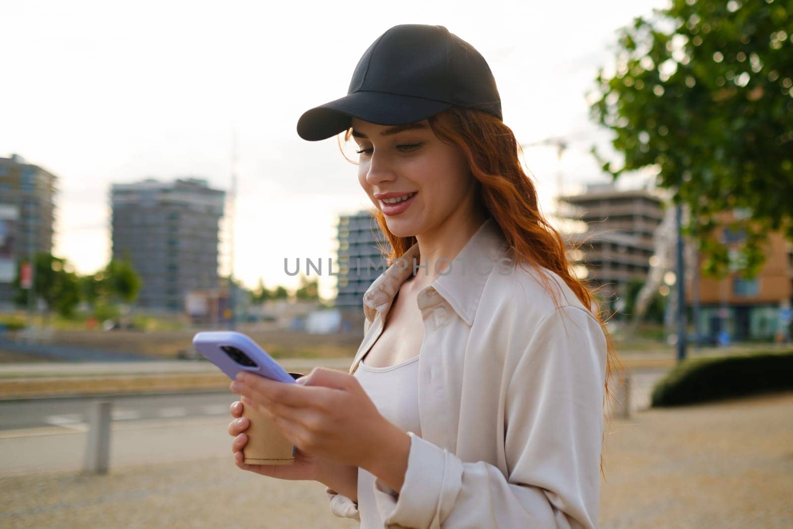 Portrait of red haired girl in casual clothes standing with a mobile phone in the street.