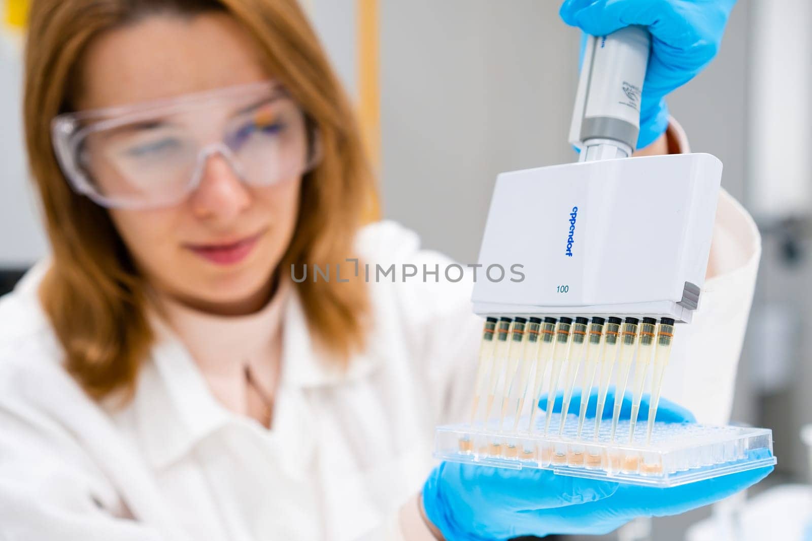 Scientist in goggles and lab coat employs a multichannel pipette Eppendorf dispenser to load microplates for immunoassay, July 2023, San Francisco, USA.