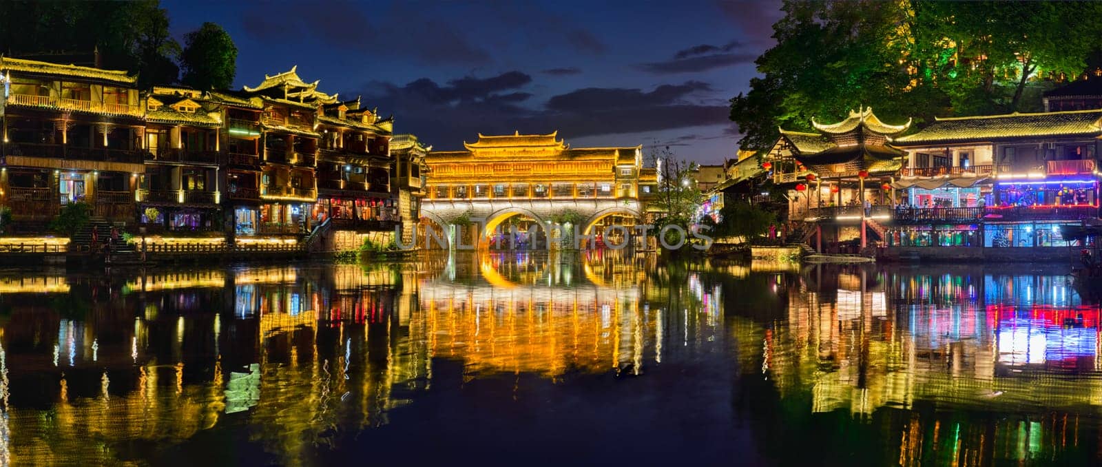 Chinese tourist attraction destination - panorama of Feng Huang Ancient Town (Phoenix Ancient Town) on Tuo Jiang River illuminated at night. Hunan Province, China