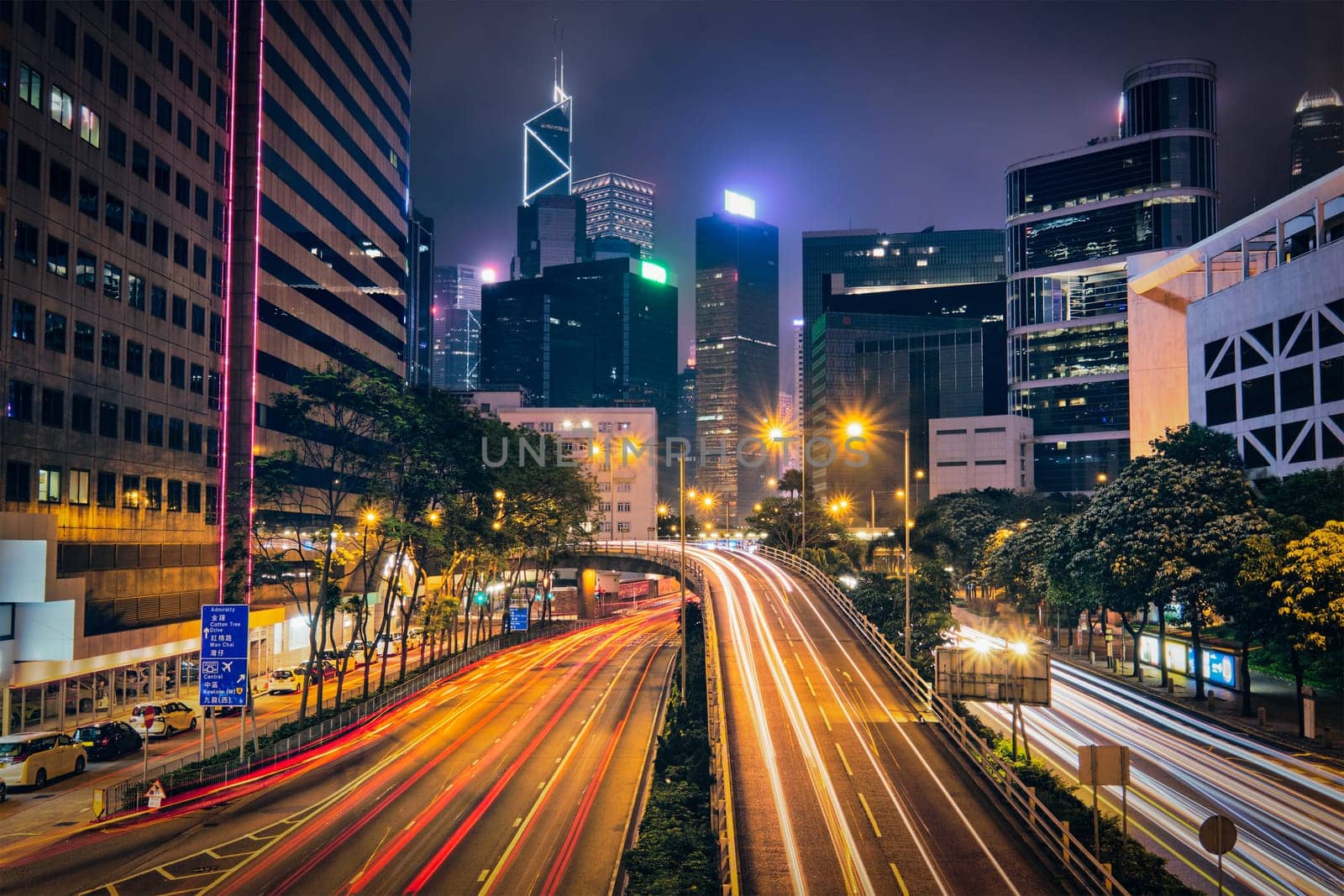 Street traffic in Hong Kong at night. Office skyscraper buildings and busy traffic on highway road with blurred cars light trails. Hong Kong, China