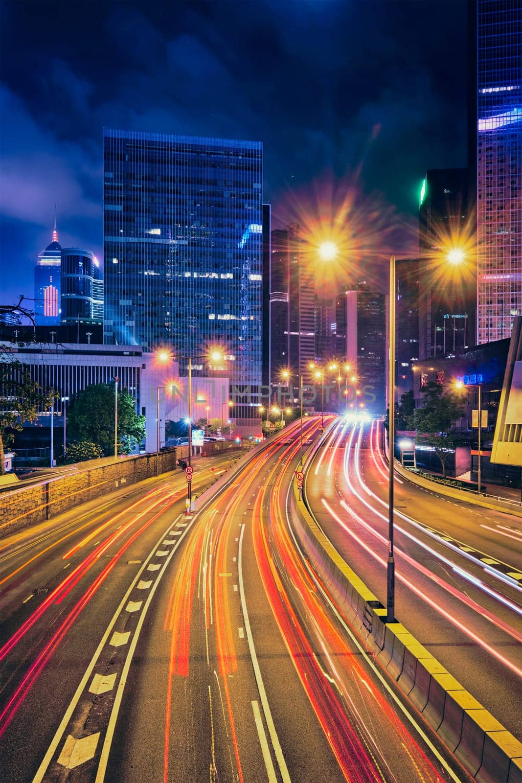 Street traffic in Hong Kong at night. Office skyscraper buildings and busy traffic on highway road with blurred cars light trails. Hong Kong, China