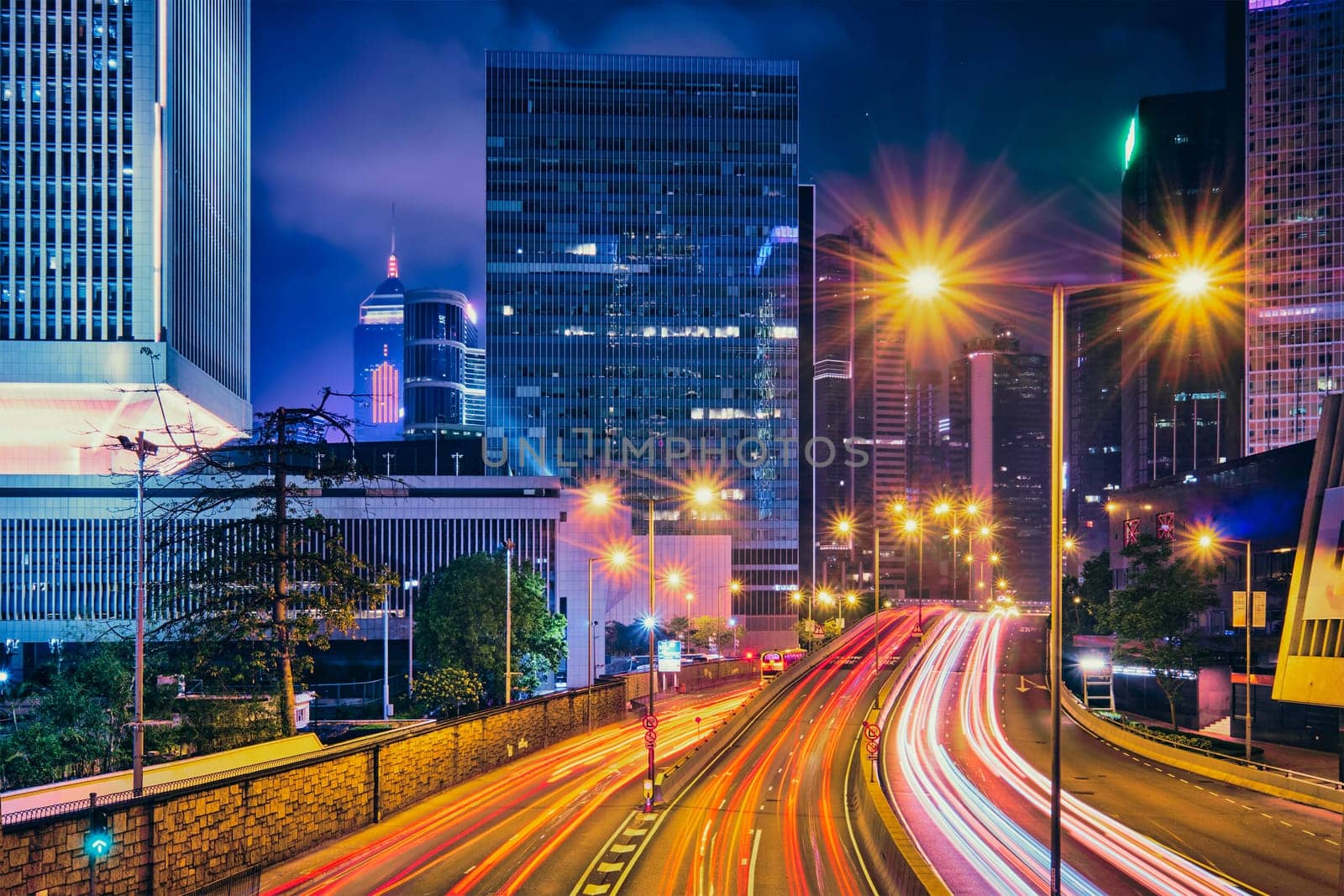 Street traffic in Hong Kong at night. Office skyscraper buildings and busy traffic on highway road with blurred cars light trails. Hong Kong, China