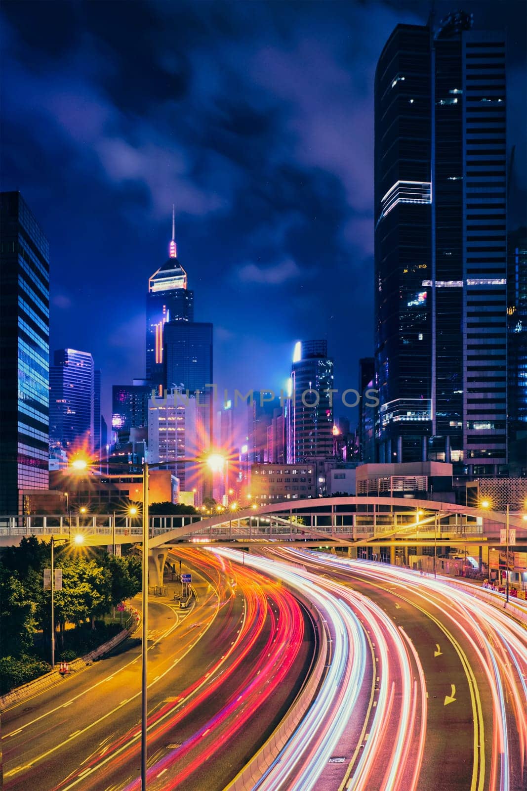 Street traffic in Hong Kong at night. Office skyscraper buildings and busy traffic on highway road with blurred cars light trails. Hong Kong, China