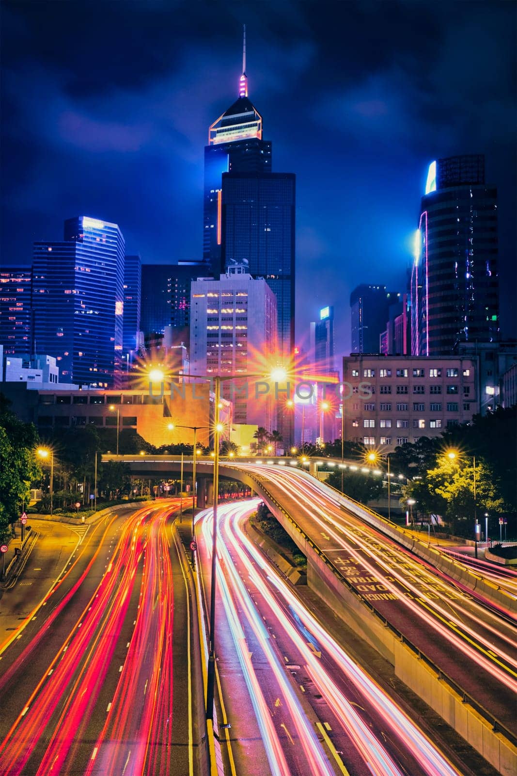 Street traffic in Hong Kong at night. Office skyscraper buildings and busy traffic on highway road with blurred cars light trails. Hong Kong, China