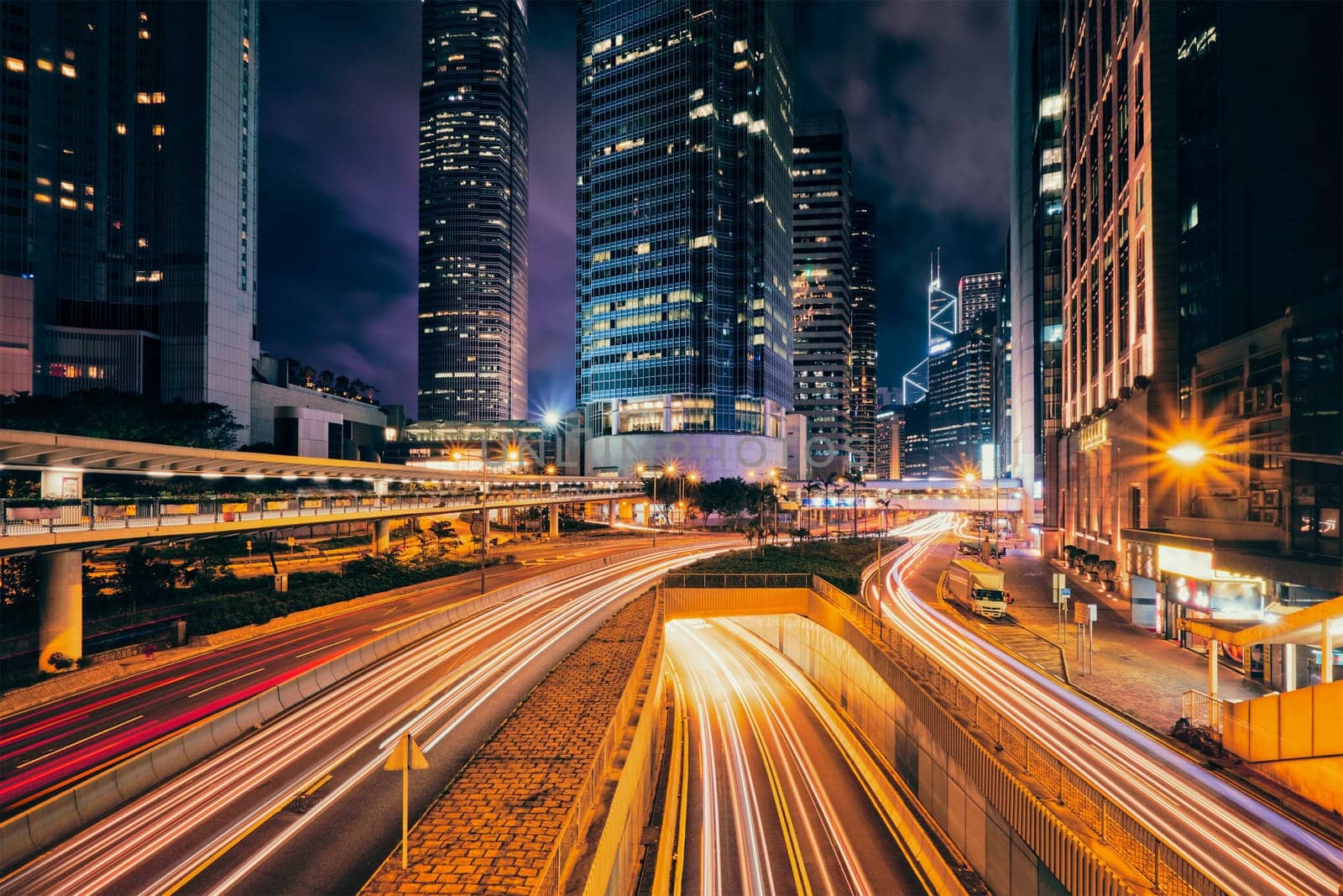 Street traffic in Hong Kong at night. Office skyscraper buildings and busy traffic on highway road with blurred cars light trails. Hong Kong, China