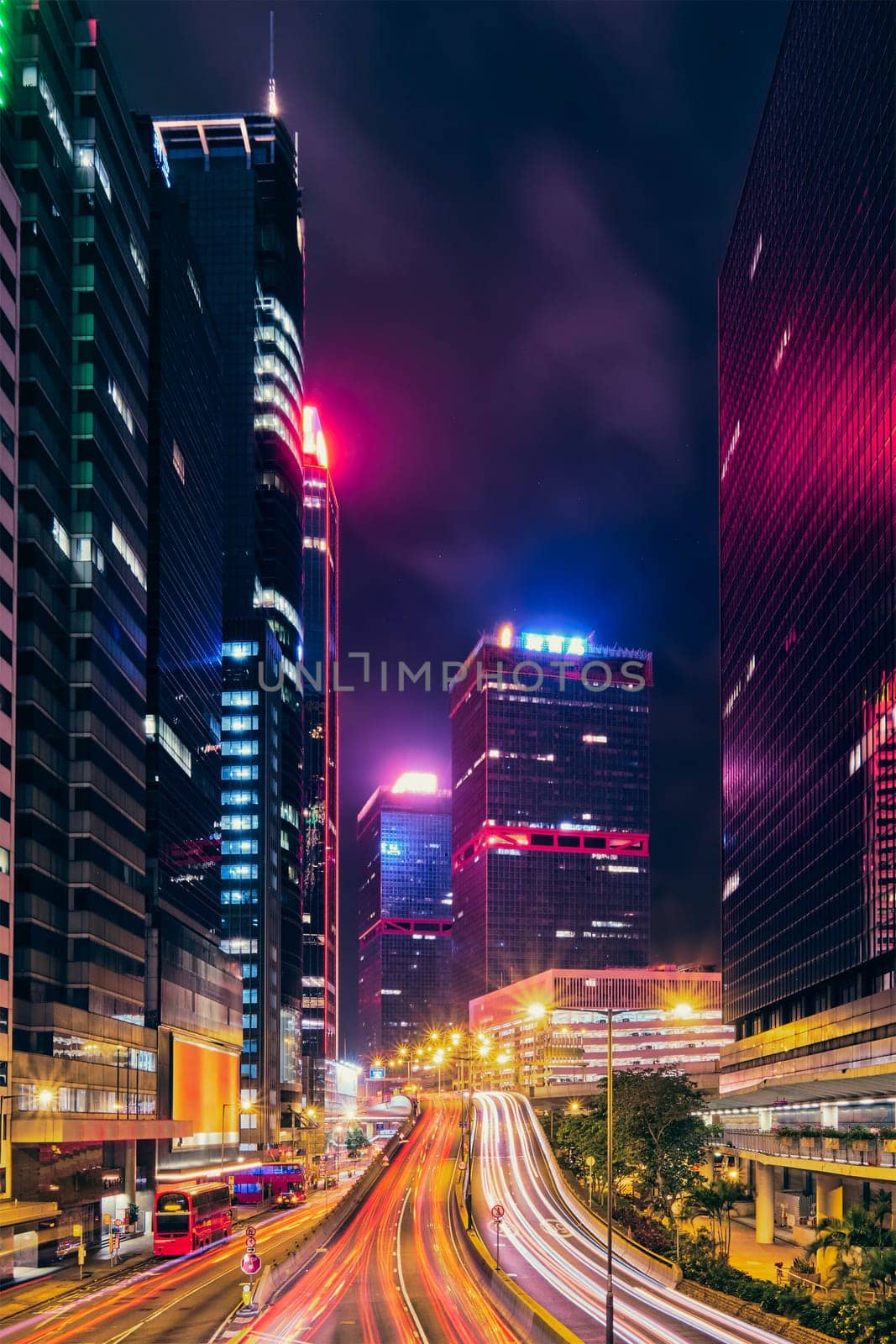 Street traffic in Hong Kong at night. Office skyscraper buildings and busy traffic on highway road with blurred cars light trails. Hong Kong, China