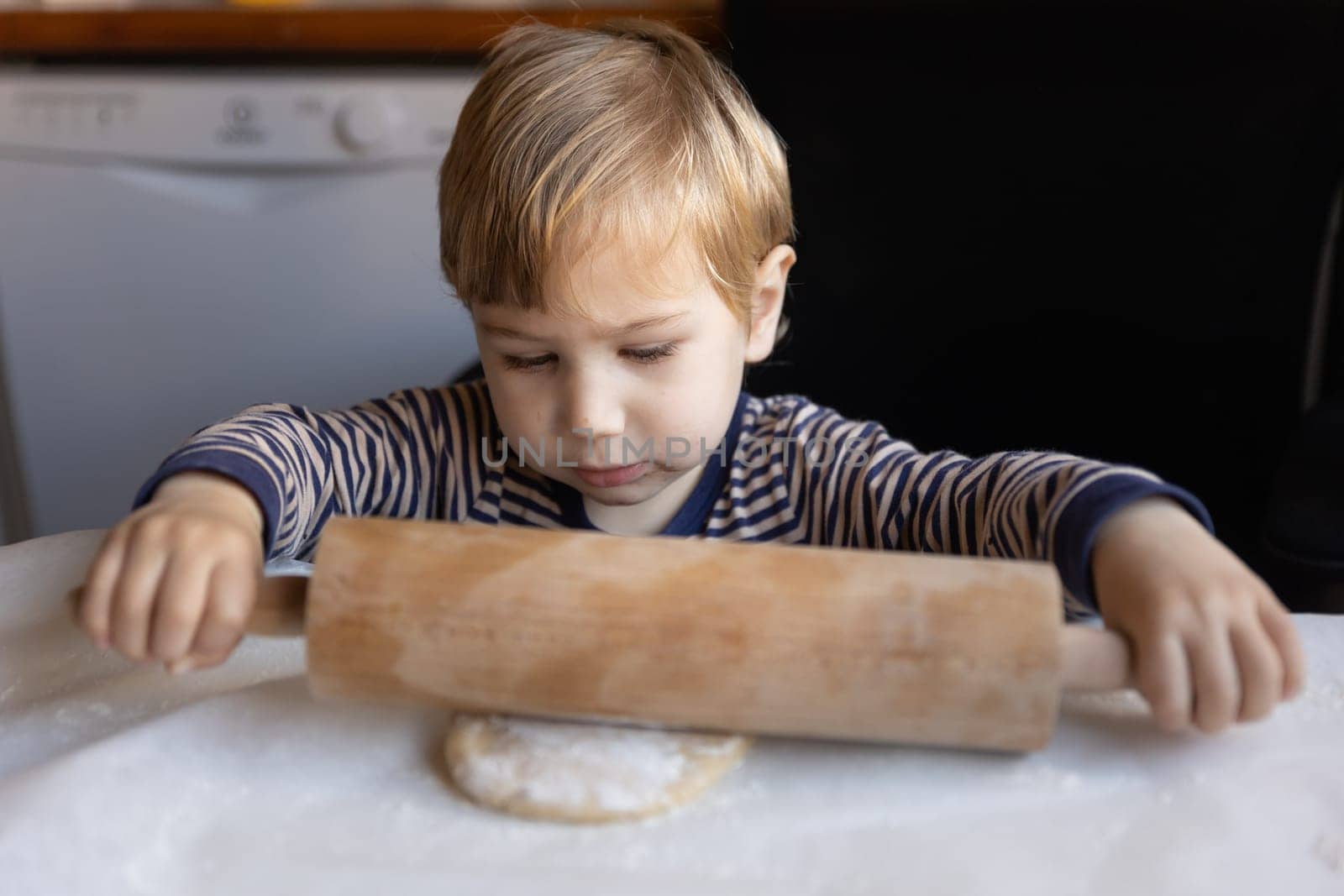 Family cooking - a little boy rolls out dough with a rolling pin. Mid shot