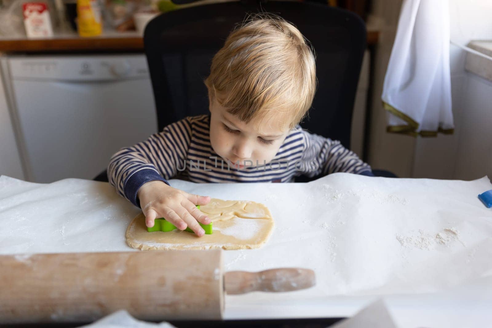Family cooking - a little boy pushes in a cutting cookie mold onto the raw dough. Mid shot