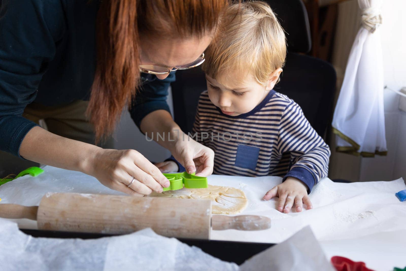 Family cooking - a woman with her little son cutting dinosaurs out of raw dough with a mold. Mid shot