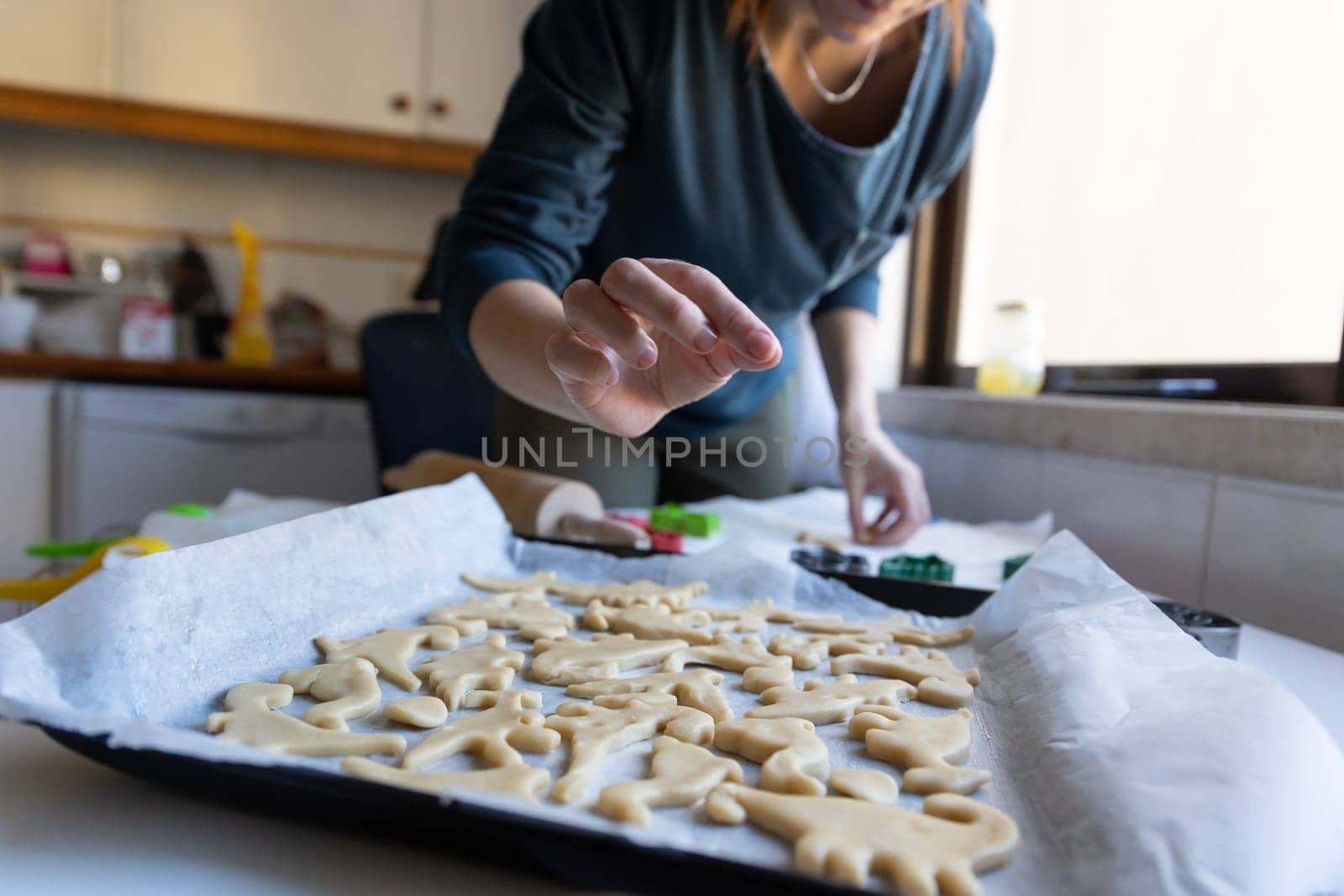 Making cookies in the shape of dinosaurs - a woman sprinkles sugar on cookie dough. Mid shot