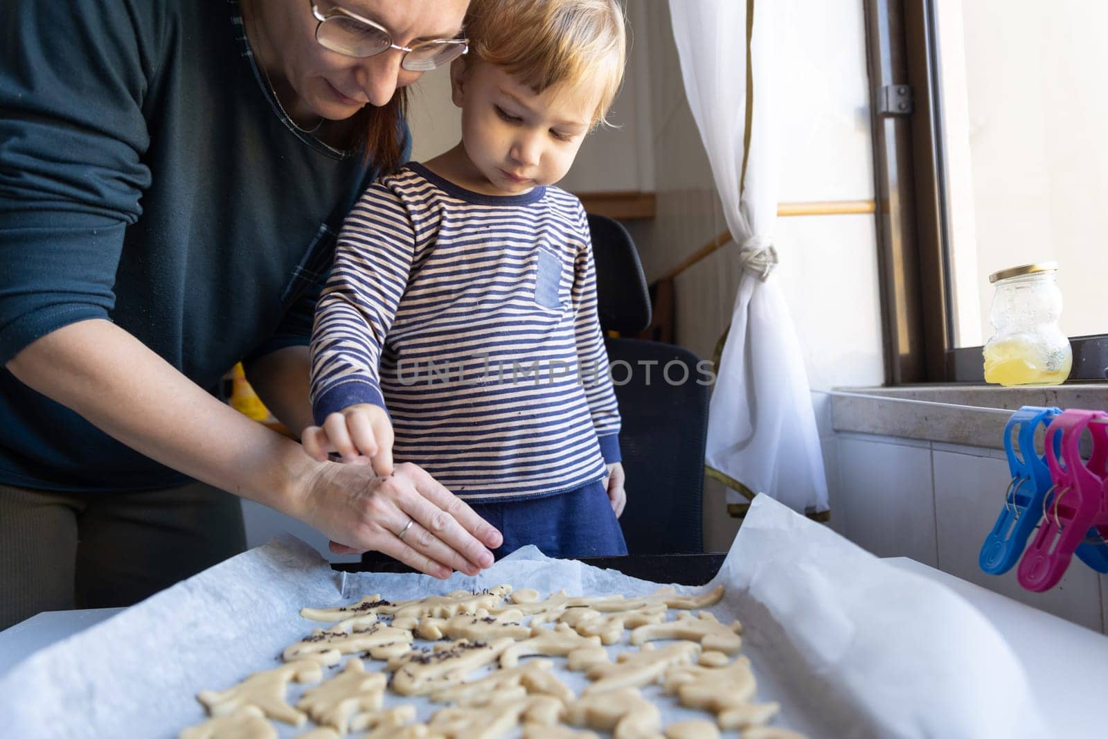 Family making cookies - a woman with her little son sprinkle poppy seed on the dough by Studia72