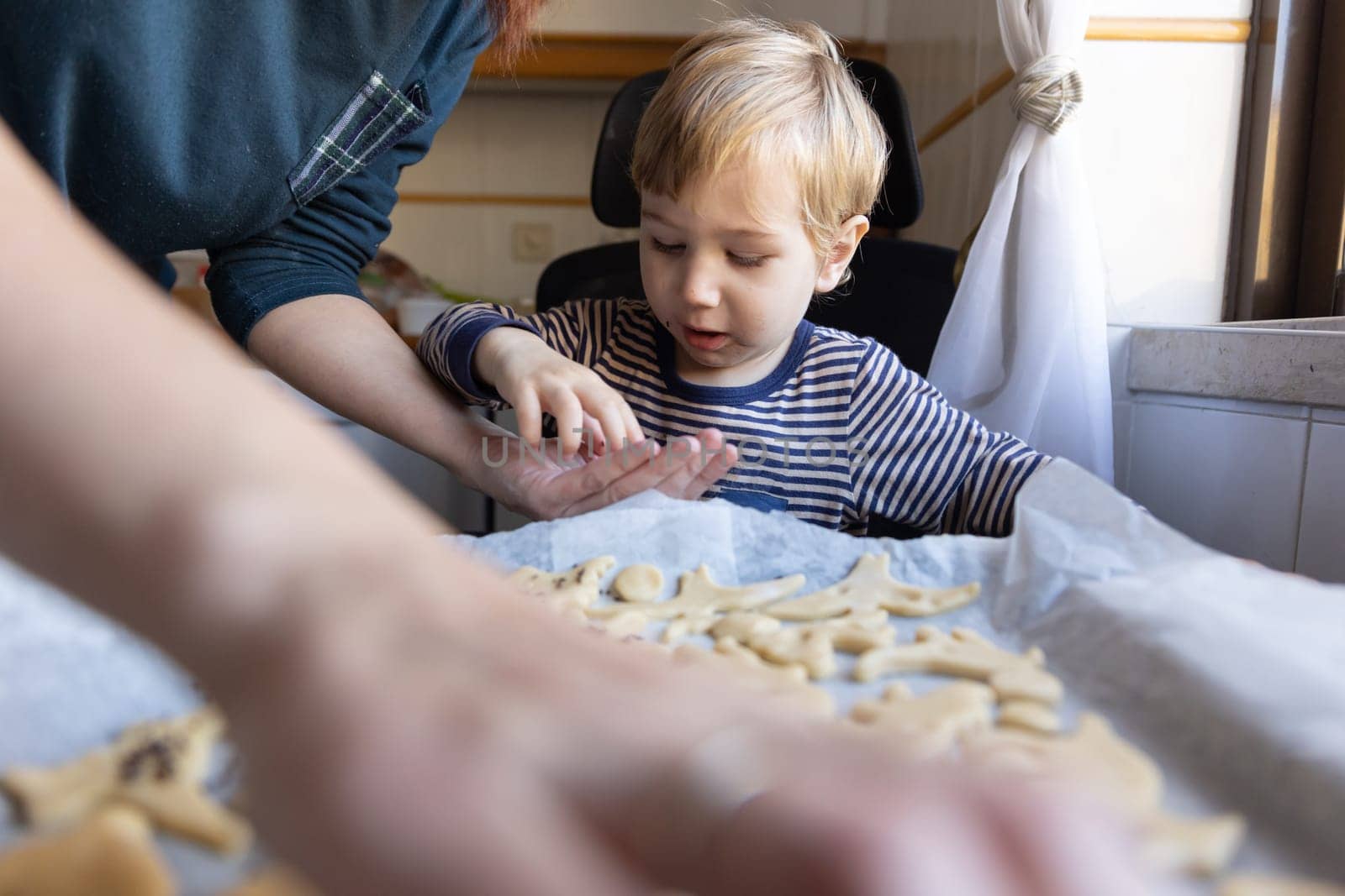 Family making cookies - a little boy takes a sprinkling from the palm of his mother. Mid shot