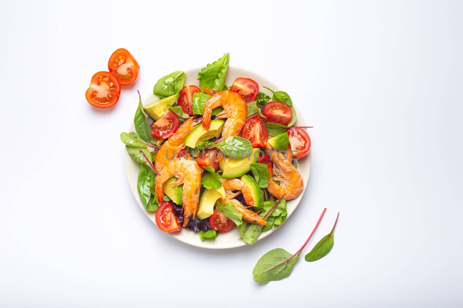 Healthy salad with grilled shrimps, avocado, cherry tomatoes and green leaves on white plate isolated on white background top view. Clean eating, nutrition and dieting concept..