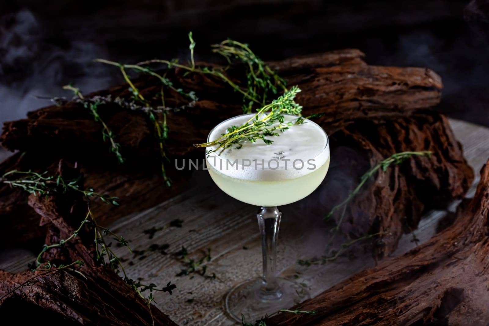 Glass of fresh green cold appetizing cocktail with froth decorated with straw and mint served on black counter by Milanchikov