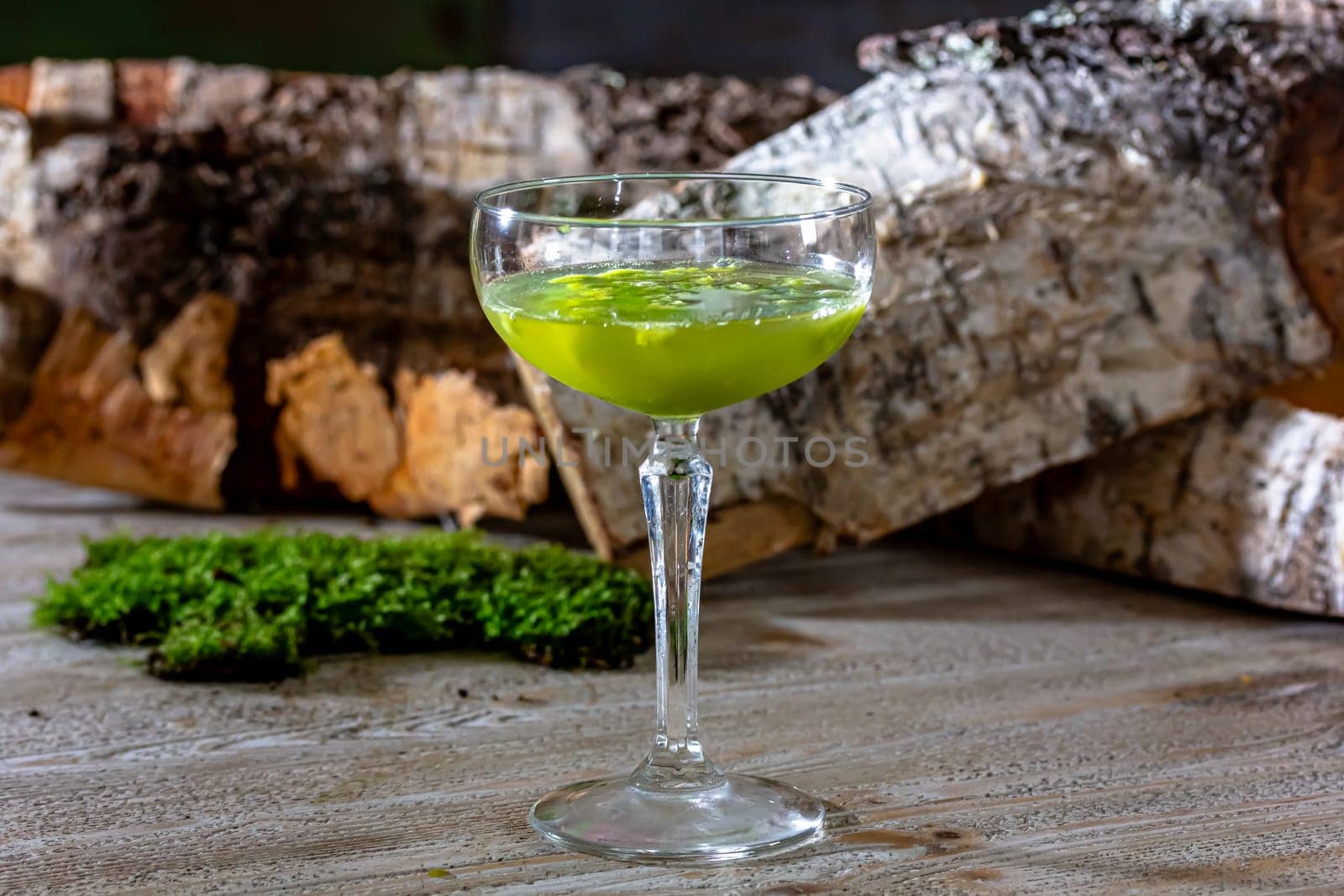 Glass of fresh green cold appetizing cocktail with froth decorated with straw and mint served on black counter.