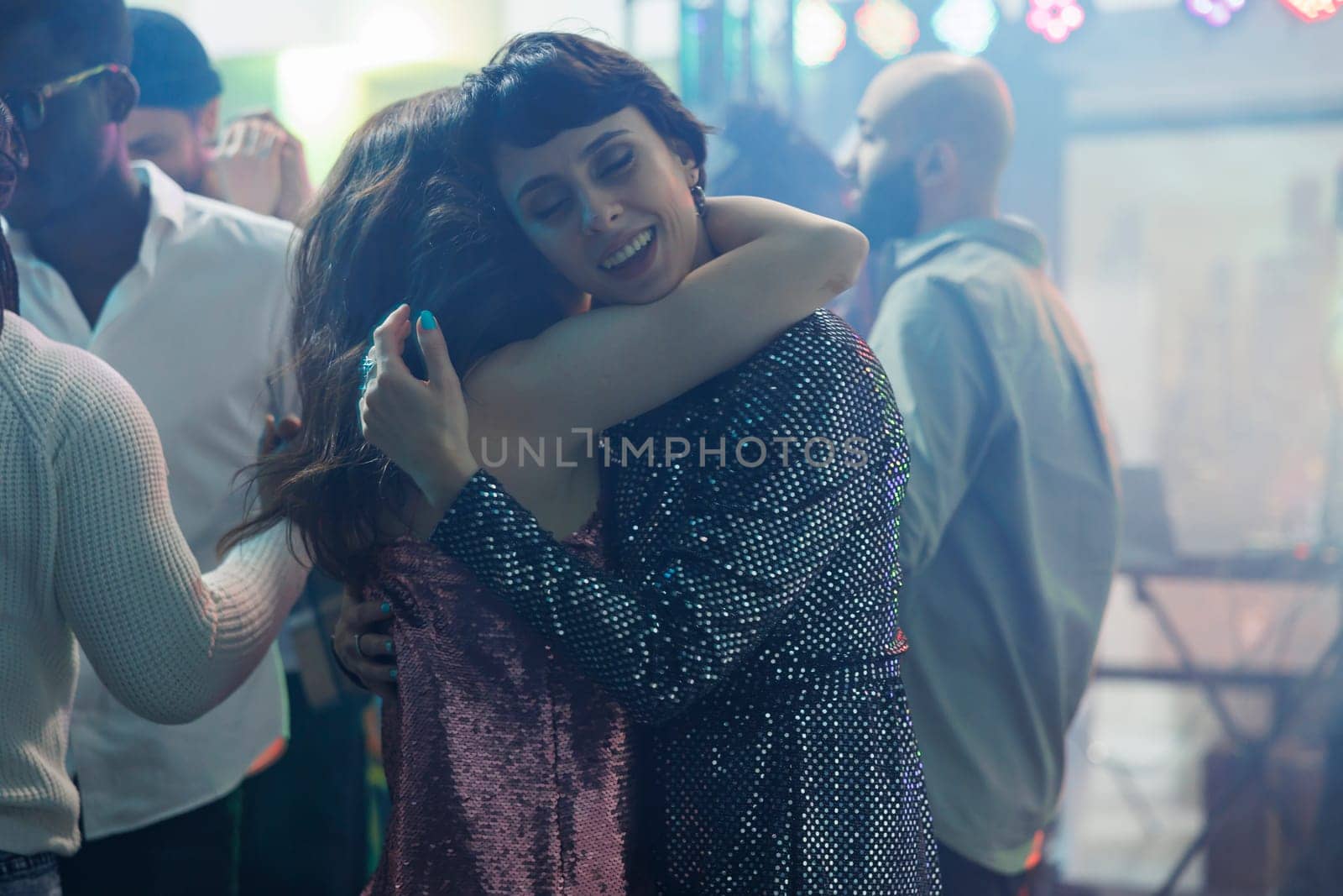 Young women hugging and dancing while attending disco party in nightclub. Romantic girlfriends couple embracing on dancefloor while clubbing and relaxing at discotheque event in club