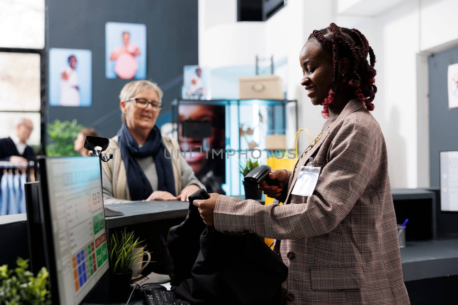 African american employee scanning blouse barcode using store scanner, discussing merchandise discount with elderly customer. Senior shopper buying fashionable clothes in boutique shop