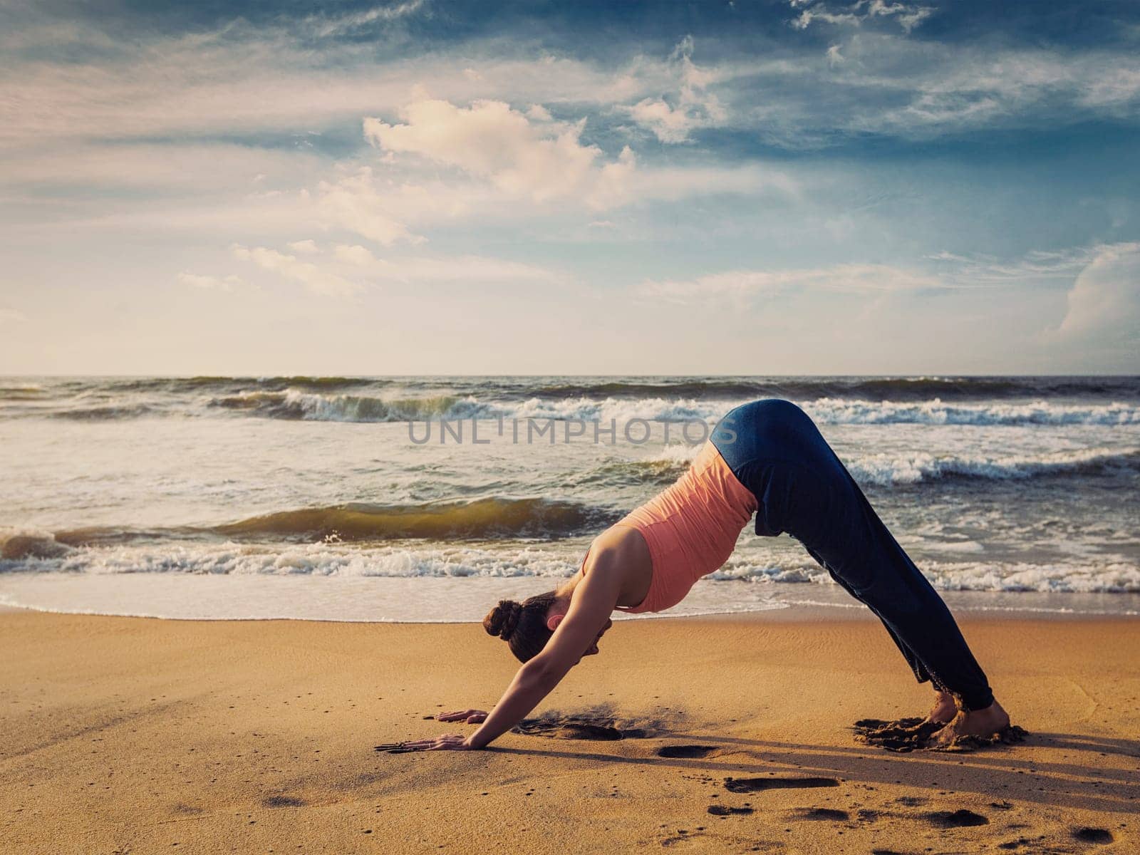 Vintage retro effect filtered hipster image of Yoga outdoors - woman doing Ashtanga Vinyasa yoga asana Adho mukha svanasana - downward facing dog - at tropical beach on sunset. Kerala, India