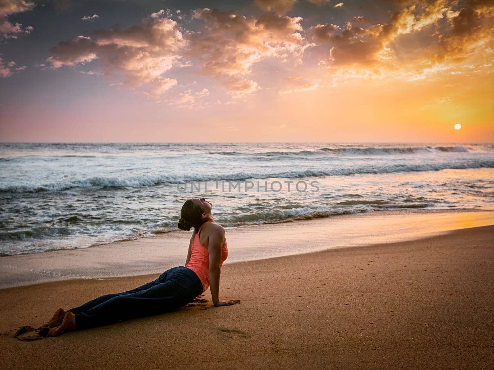 Woman practices yoga asana Urdhva Mukha Svanasana at the beach by dimol