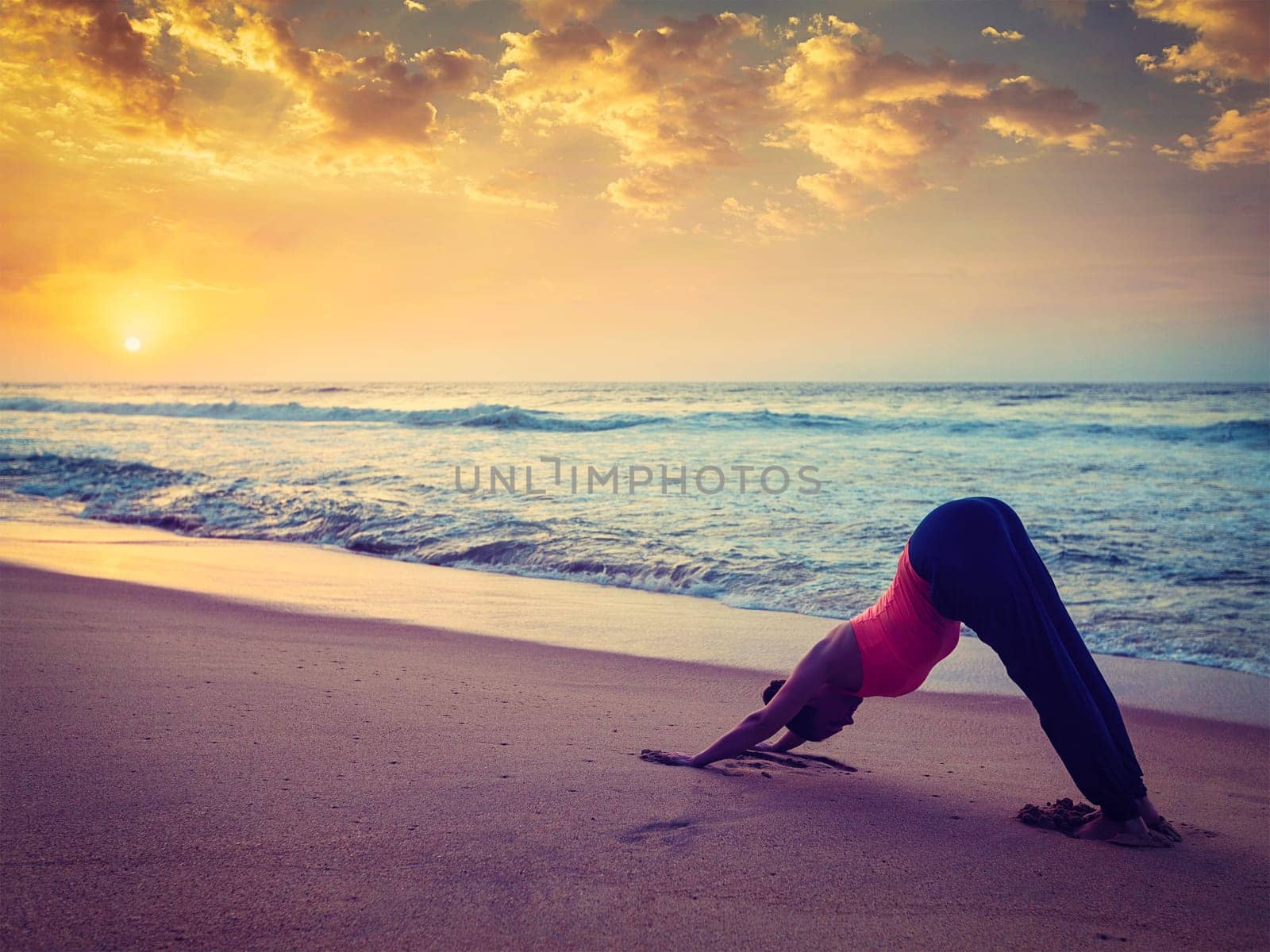 Young sporty fit woman doing yoga at beach on sunset by dimol