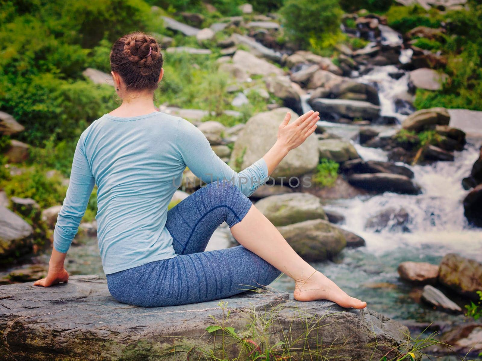 Woman doing Ardha matsyendrasana asana outdoors by dimol