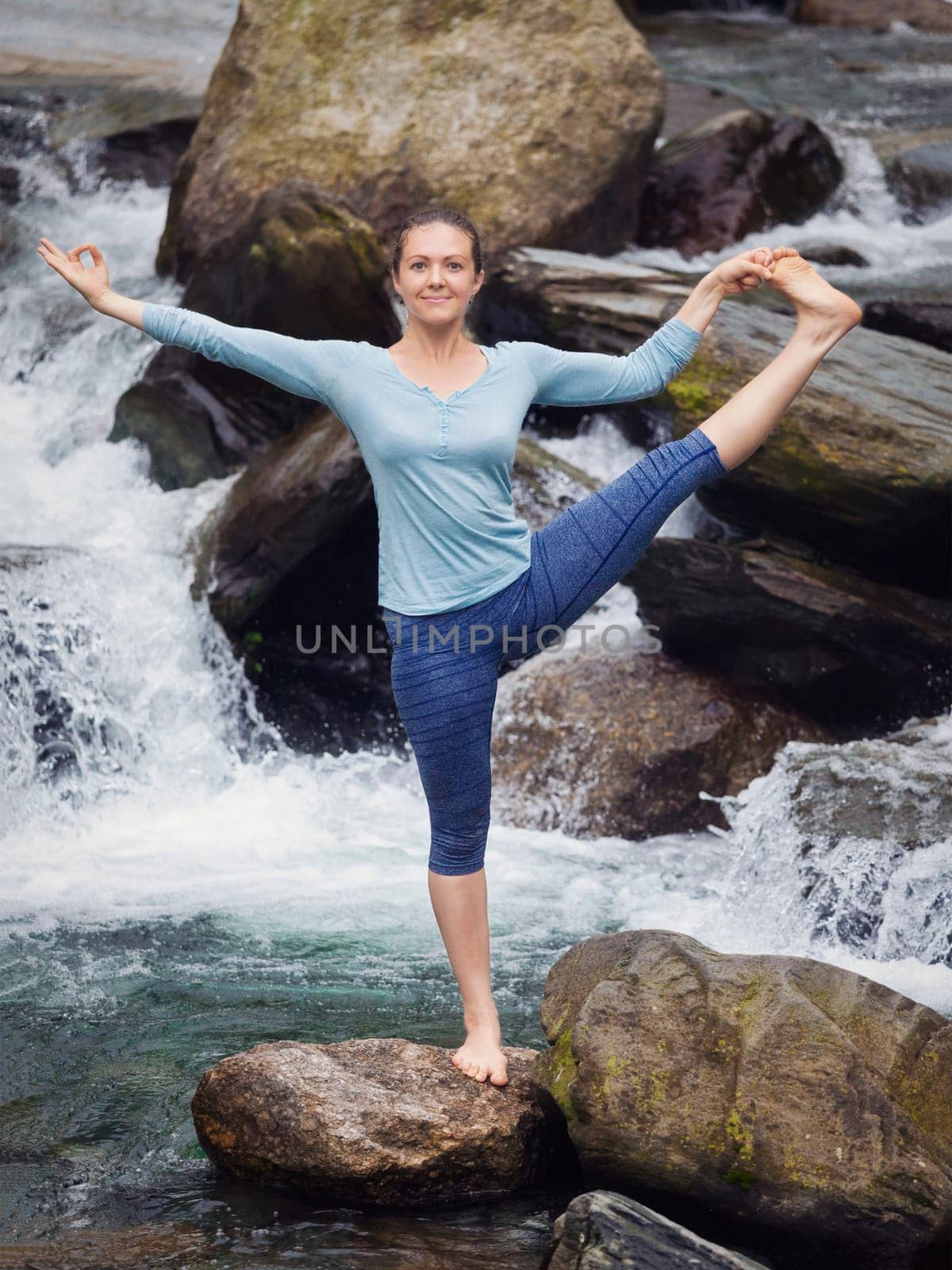 Yoga outdoors - woman doing Ashtanga Vinyasa Yoga balance asana Utthita Hasta Padangushthasana Extended Hand-To-Big-Toe Pose position outdoors at waterfall. Vintage retro effect filtered hipster style