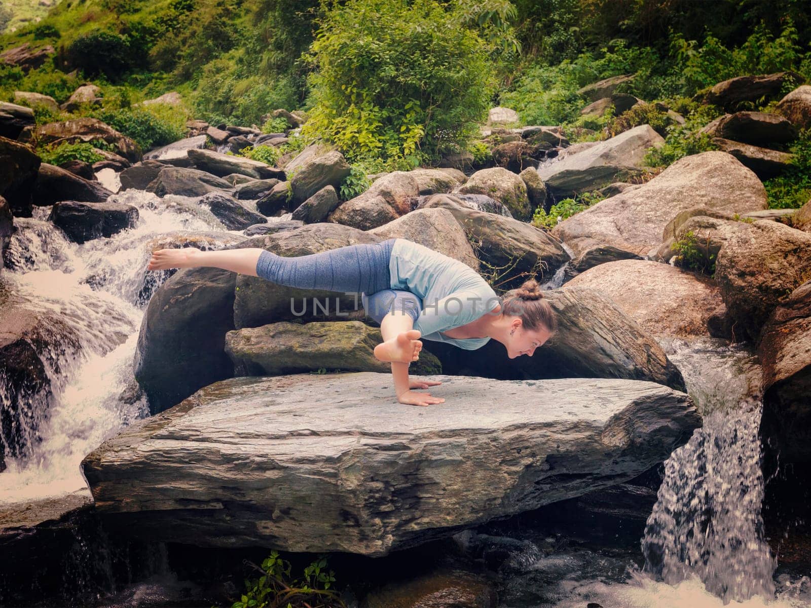 Young sporty fit woman doing yoga oudoors at tropical waterfall by dimol